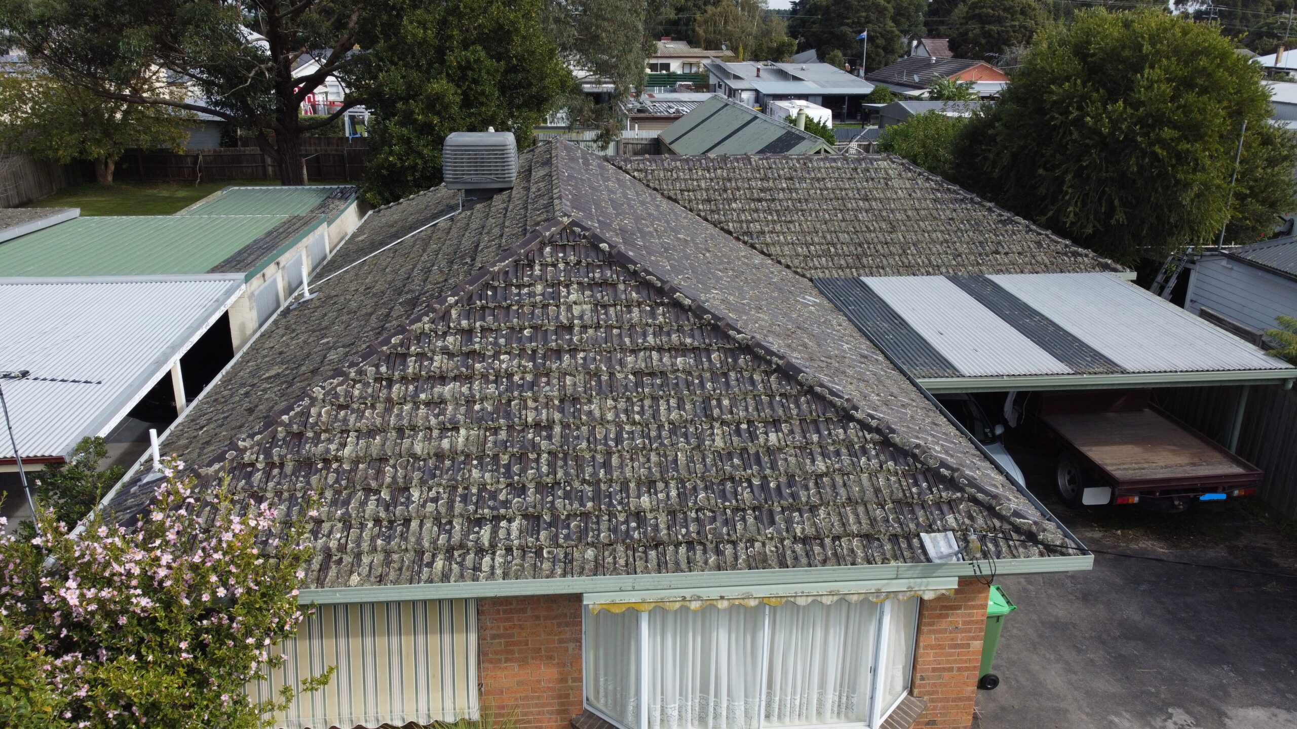 Aerial view of a Melbourne suburban home with an old tiled roof showing moss and lichen growth, illustrating common roofing issues addressed by Top Glaze Roofing Systems’ repair and restoration services.