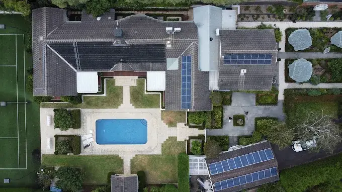 Aerial view of residential solar panel installations on multiple rooftops surrounding a central pool.